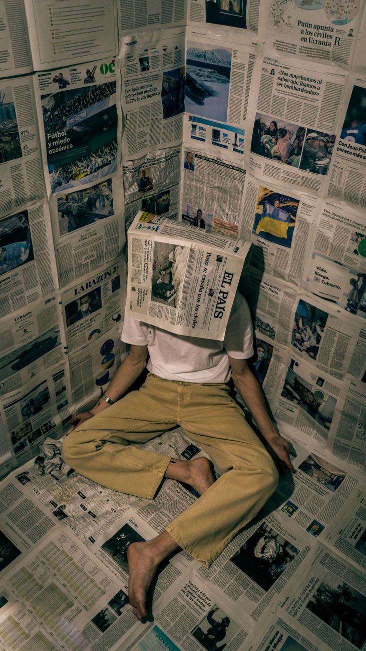 person sits in a corner with a newspaper over their head